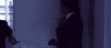 a man in a suit and tie is standing in a dark room adjusting his tie