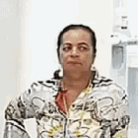 a woman in a floral shirt is standing in front of a machine and looking at the camera .