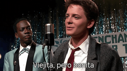 a man in a suit and tie stands in front of a microphone with the words " viejita pero bonita " below him