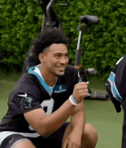 a man in a carolina panthers jersey is sitting on the ground and smiling .