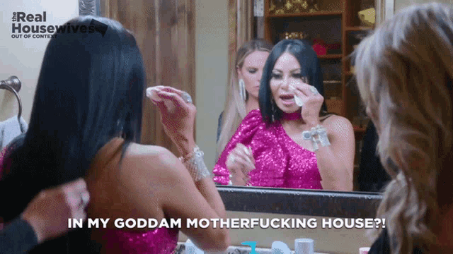 a woman wipes her eyes in front of a mirror with the words in my goddam motherfucking house on the bottom