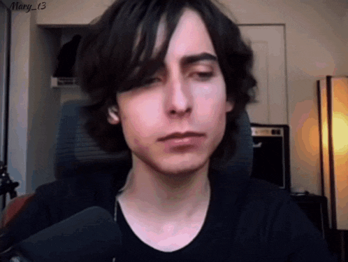 a young man with long dark hair is sitting in a chair .