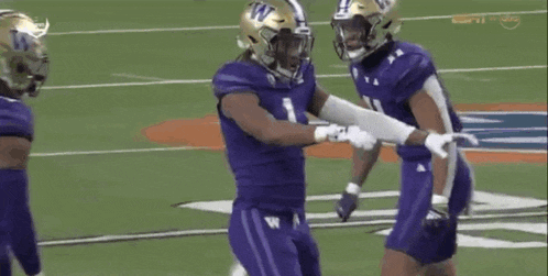 a football player in a purple uniform is kneeling down on the field while another player holds his arm .