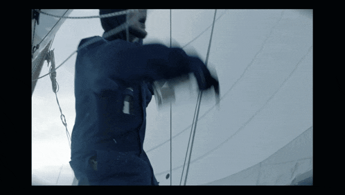 a person in a blue jacket is standing on a sailboat