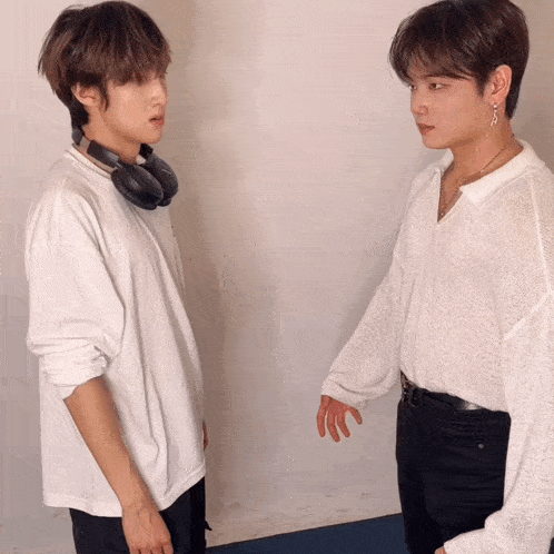 two young men standing next to each other one wearing headphones around his neck