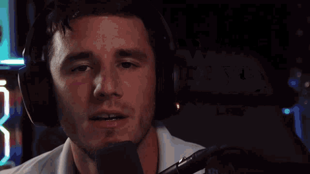 a man wearing headphones stands in front of a microphone with the words " what are you doing " behind him