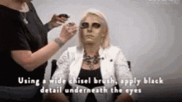 a woman is getting her face painted with a wide chisel brush .