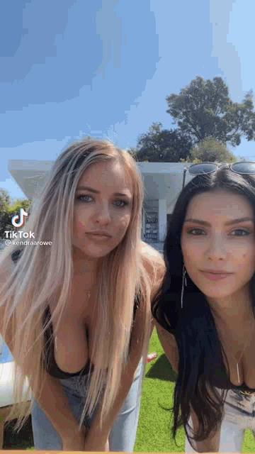 two women are standing next to each other on a lush green field . one of the women is wearing a black bra .