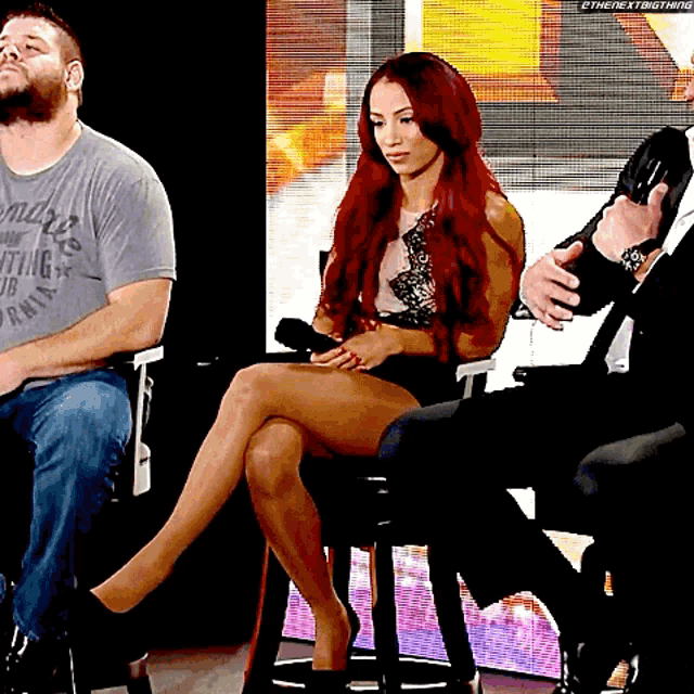 a woman with red hair is sitting in a chair with her legs crossed in front of a group of people