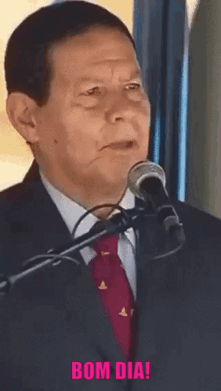 a man in a suit and tie is speaking into a microphone with the words bom dia written below him