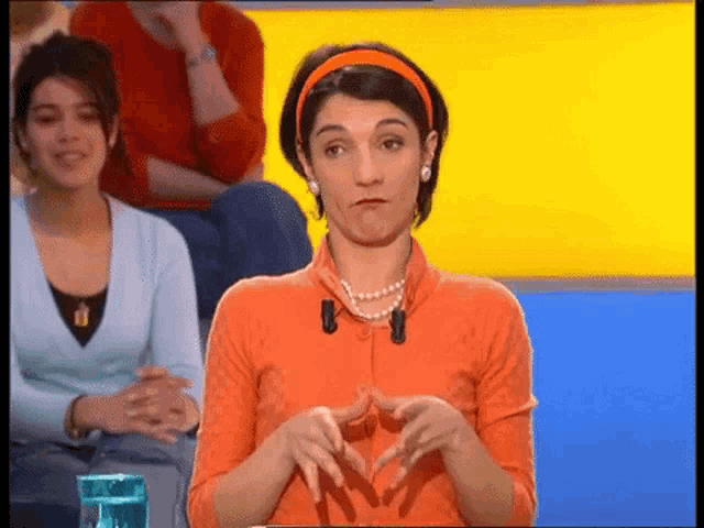 a woman wearing an orange shirt and a pearl necklace is making a funny face