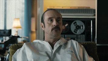 a man with a mustache is sitting in a chair wearing a white shirt that says " florida " on it