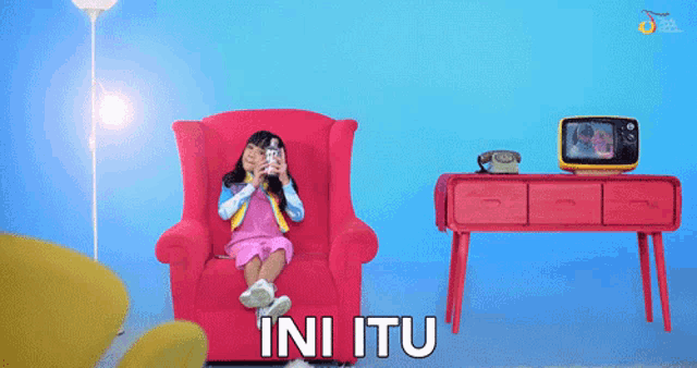a little girl sitting in a red chair with the words ini itu written on the bottom