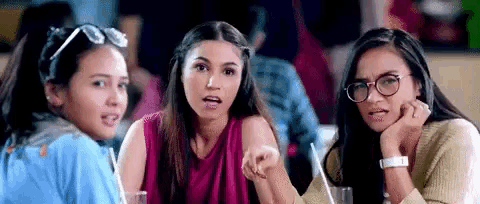 three young women are sitting at a table talking to each other .