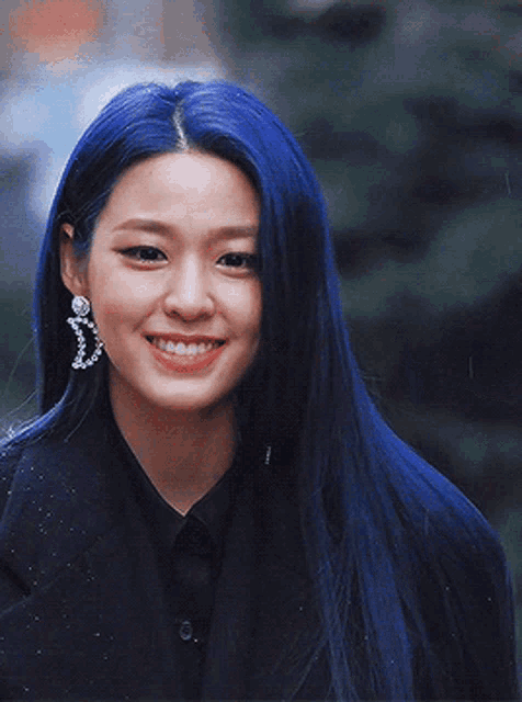 a woman with long blue hair is wearing a black shirt and earrings
