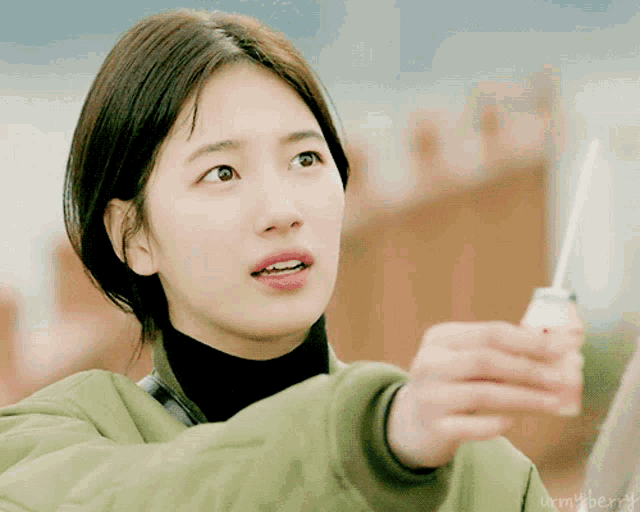 a woman in a green jacket is holding a container of something