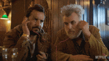 two men sitting at a table with a netflix logo on the bottom