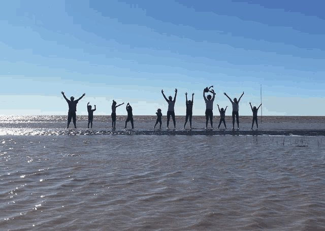 a group of people are jumping into the water with their arms in the air