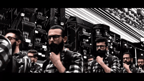 a group of men wearing plaid shirts and glasses are standing in a room with a lot of computers .