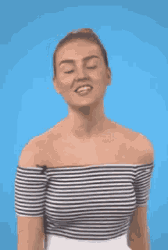 a woman wearing a striped off the shoulder top is standing in front of a blue background .