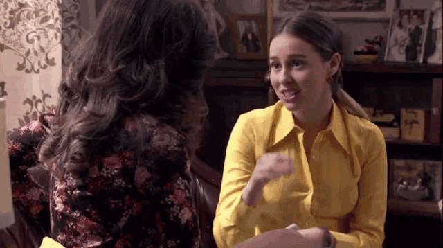 a woman in a yellow shirt is talking to another woman in a black dress