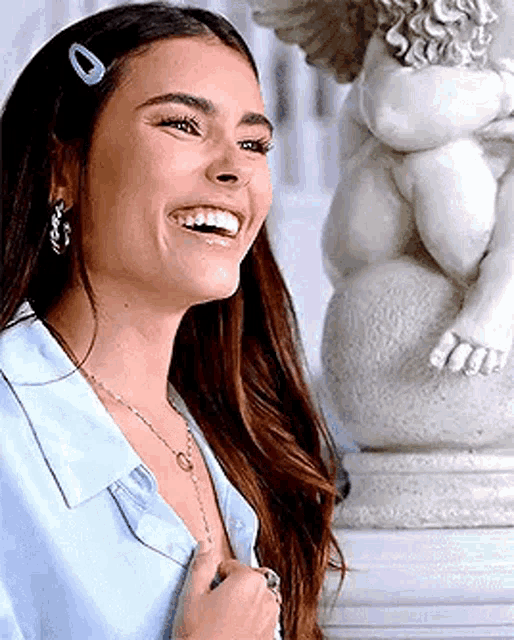 a woman in a blue shirt is smiling in front of a statue of an angel .