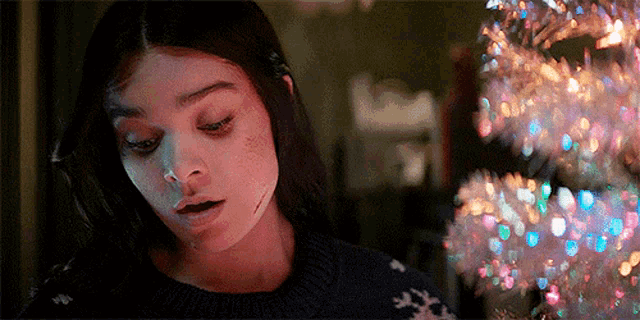 a woman with a scar on her face is standing in front of a christmas tree with lights .