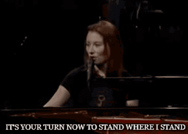 a woman singing into a microphone with the words " it 's your turn now to stand where i stand " above her