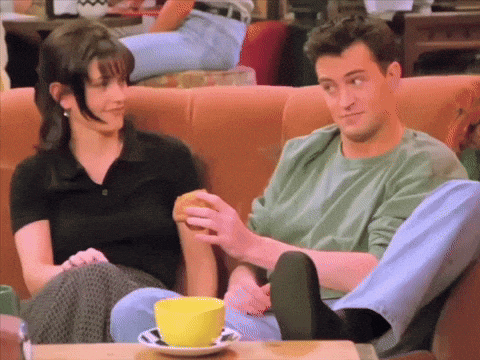 a man and a woman are sitting on a couch and the man is holding a hamburger