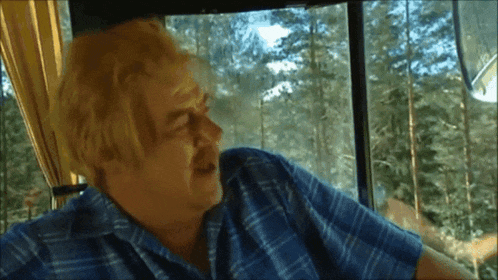 a man in a blue plaid shirt is looking out of a window