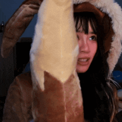 a woman wearing bunny ears is holding a stuffed animal behind her face .