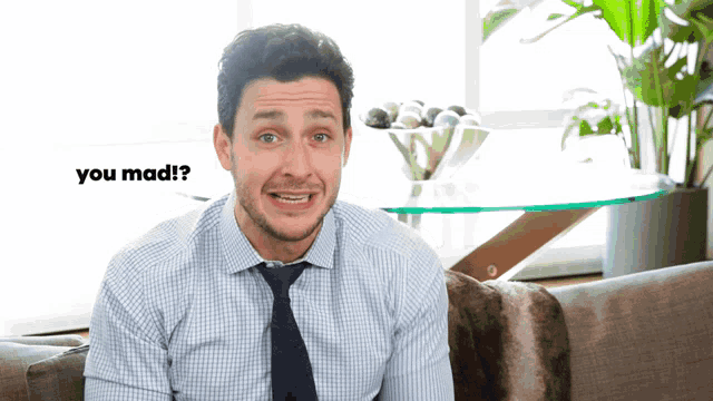 a man sitting on a couch with the words " you mad " behind him