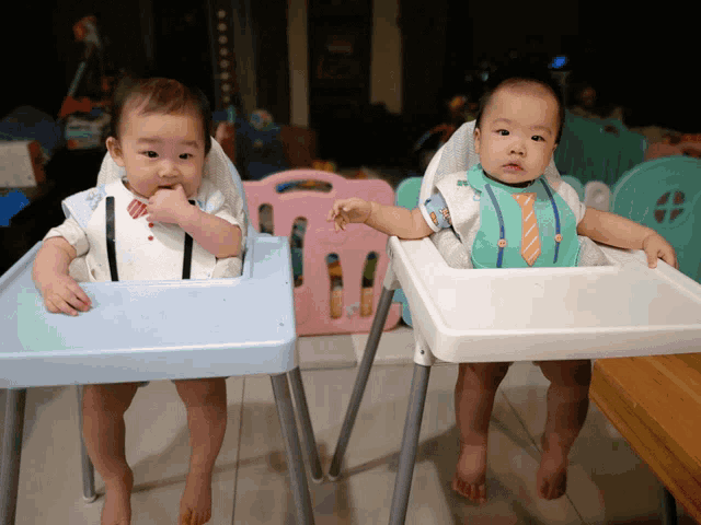 two babies are sitting in high chairs and one has a tie on