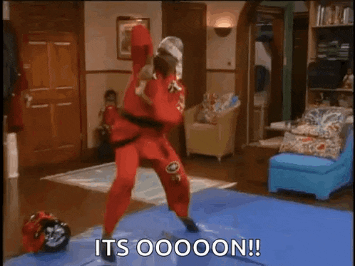 a man in a red karate outfit is standing on a blue mat in a living room .