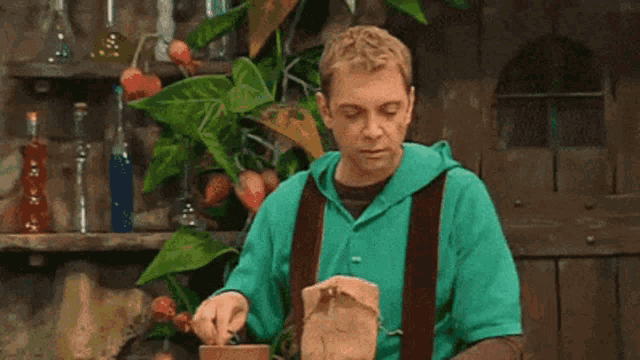 a man in a green hoodie is dancing in front of a plant