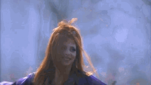 a woman with long red hair is wearing a purple jacket and a purple shirt .