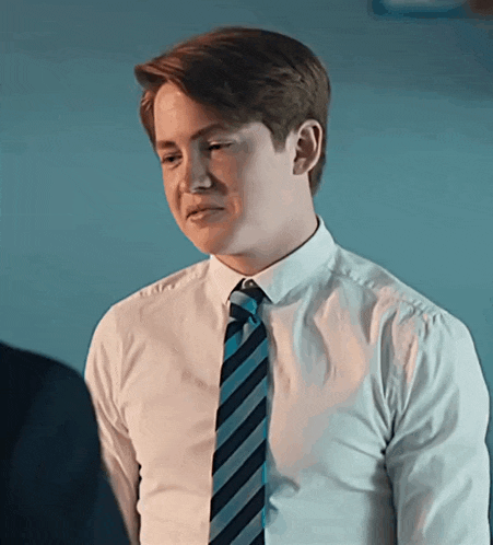 a young man wearing a white shirt and blue striped tie looks to the side