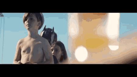 a boy without a shirt is standing next to a girl and a man in a batman costume .