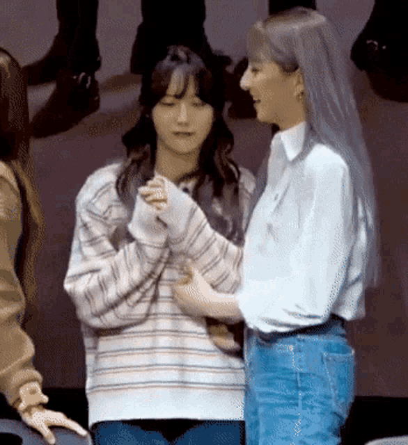 two women are standing next to each other holding hands and looking at each other .