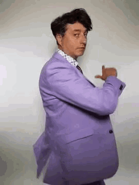 a man in a purple suit and tie is dancing and making a funny face .