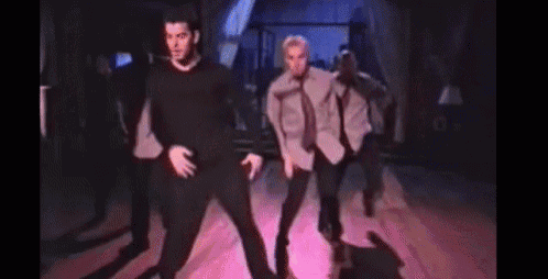 a group of men are dancing in a room with a pink light behind them .