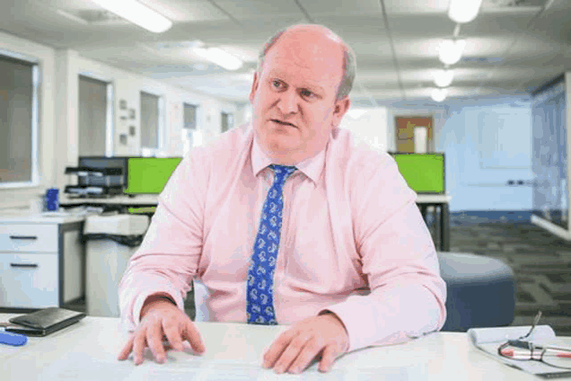 a man is sitting at a desk in an office wearing a pink shirt and blue tie .