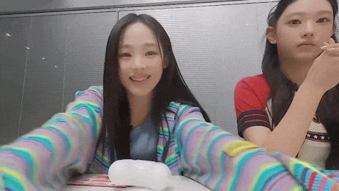 two girls are sitting at a table and one is wearing a striped shirt