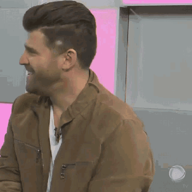 a man with a beard wearing a brown jacket and a white shirt is smiling .