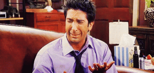 a man in a purple shirt and tie is crying while sitting on a couch in a living room .