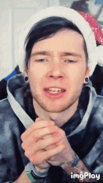 a man wearing a santa hat is making a funny face with his hands folded