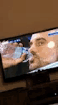 a man with a beard is drinking water from a bottle on a tv screen