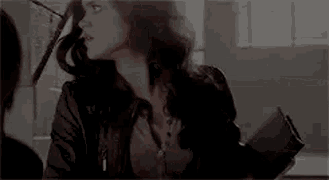a woman in a leather jacket is standing next to a man in a room holding a book .