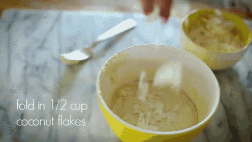 a yellow bowl filled with coconut flakes next to a spoon