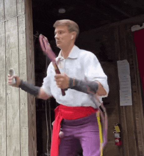 a man in a white shirt and purple pants holding a whip
